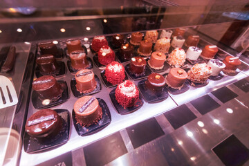 Elegant luxury chocolate desserts and artisan pastries displayed in glass cabinet at gourmet confectionery shop. Premium sweet treats showcasing fine craftsmanship and culinary artistry.