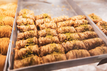 Close-up of freshly made, golden-brown baklava rolls with a sticky syrup glaze and a generous...
