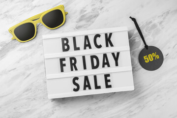 Black friday sale word on lightbox with sale tag and sunglasses on marble table