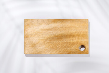 Empty cutting board on a white background with leaf shadows