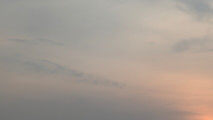 A vast sky filled with soft, wispy clouds. The color palette transitions from a muted gray at the...