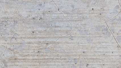 A close-up of a weathered, light gray concrete wall. The surface is covered in a network of fine...