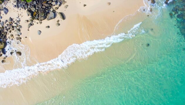 Aerial view of a pristine beach with turquoise water gently lapping the sandy shore and rocks - Powered by Adobe