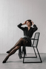 model showcases a chic black outfit while sitting gracefully on a wire chair in a contemporary studio, exuding confidence and fashion-forward vibes