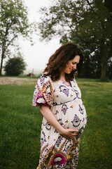 Fototapeta premium Pregnant mom smiles down happily at baby bump in floral dress