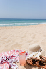 Straw hat, sandals, towel, and cold drink on sandy beach
