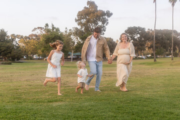 Obraz premium Young family running across grass field during summer sunset
