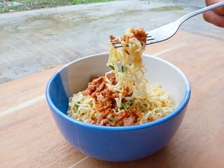 a bowl of instant noodles topped with chopped chicken, spring onions and fried shallots on a wooden...