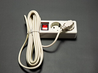 A coiled power cord is connected to a white power strip which has an on/off switch, positioned on a plain dark gray surface,creating a practical and minimalistic scene.