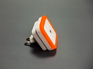 The image captures a modern, angular white and orange nightlight on a grey surface, its sleek design offering a blend of functionality and ambient lighting.