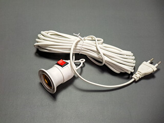 Arrangement of white electrical components includes a light bulb socket with red switch, cord neatly coiled and plug resting on a plain, muted gray surface.