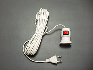 A coiled white electric cord with a plug and a switched bulb socket is seen on a plain grey background, illustrating an everyday home wiring component in a functional setting.