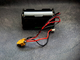 A battery pack with red and black wires leading to a yellow connector, resting on a textured grey surface, showcasing electrical components for power and connectivity.