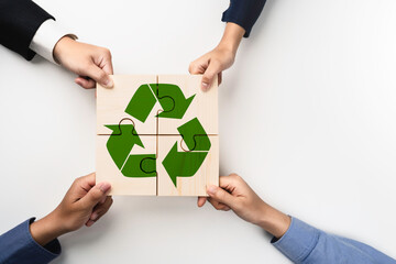 Hands assembling wooden puzzle pieces with a green recycling symbol for Reduce, reuse, recycle....