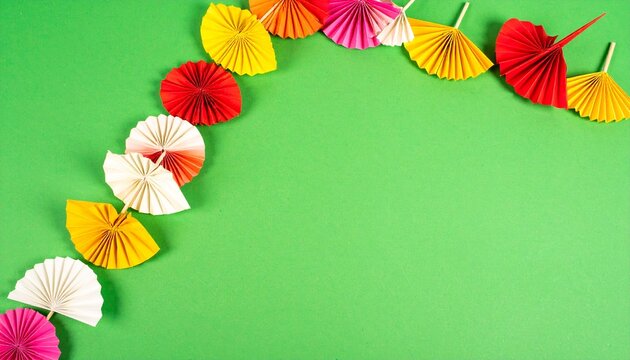 Colorful paper fan decorations forming a curved border on a bright green background with copy space.