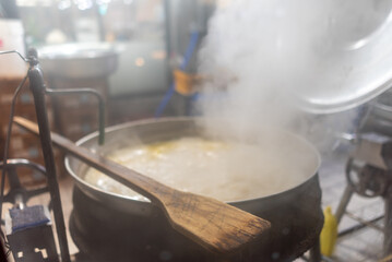A large pot of boiling soup or stew on a stove, steam rising, wooden spoon resting on the edge