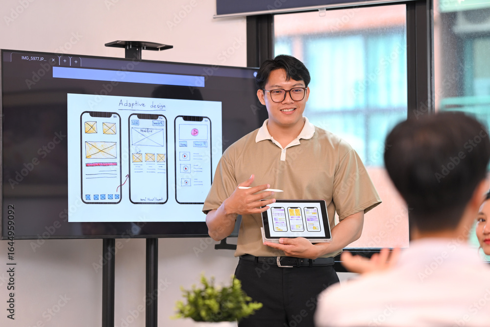 Poster man explaining mobile app wireframes on a screen while holding a tablet, during team meeting