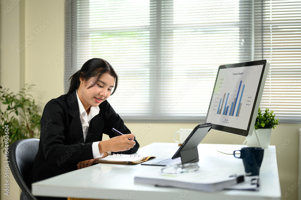 Poster businesswoman analyzing bar charts and writing in a notebook during a busy work session