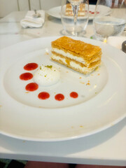 Elegant dessert plate featuring a classic mille-feuille with layers of crispy puff pastry and creamy filling, accompanied by whipped cream and dots of raspberry coulis
