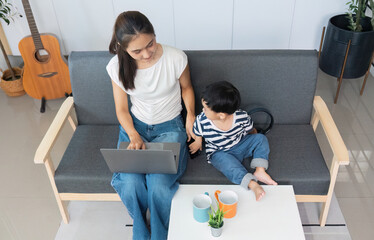 Mother multitasking with laptop while son engages nearby