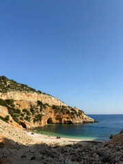Naklejka premium Scenic coastal view of a serene beach with rocky cliffs and clear blue water in sunny weather