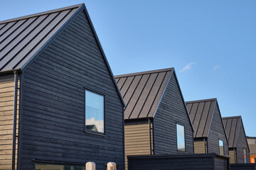 Modern black wooden houses with gabled roofs and zinc roofs in Viken, Sweden, under a bright summer sky