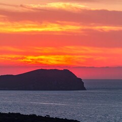 Vibrant sunset over a silhouetted island and calm sea