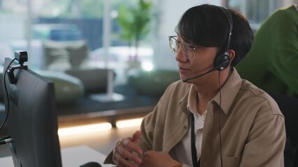 Focused young asian male operator provides diligent customer support from modern call center, professional representative wearing headset assists client during call - Powered by Adobe