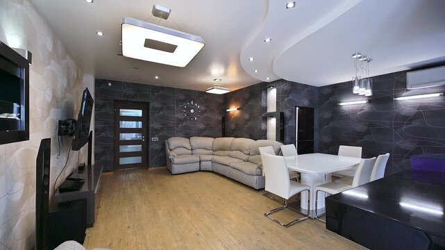 Modern living space with a corner sofa, white dining set, and a media center. Walls have a dark, patterned design. The lighting fixtures are contemporary and bright