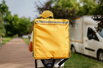 Delivery worker with yellow backpack walks on path.