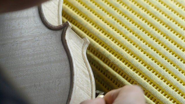 Skilled craftsman carefully sanding wooden violin body, highlighting intricate woodworking techniques in musical instrument making