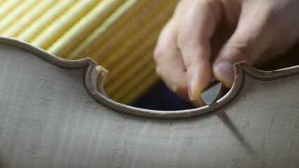Experienced luthier carefully carving intricate f hole on wooden violin surface, demonstrating meticulous woodworking skills and musical instrument crafting expertise