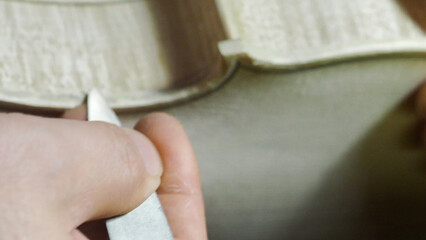 Skilled craftsman carefully carving wooden piece for violin, revealing intricate lutherie techniques with focused hand movements