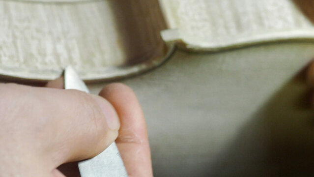 Skilled craftsman carefully carving wooden piece for violin, revealing intricate lutherie techniques with focused hand movements