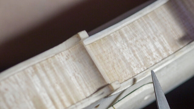 Skilled craftsman carefully carving intricate purfling detail on violin belly, highlighting woodworking precision and traditional lutherie craftsmanship