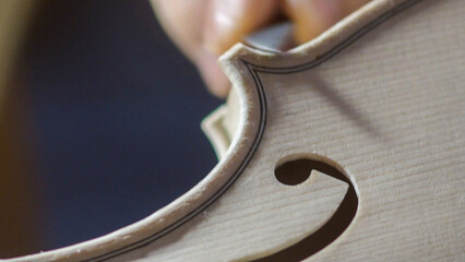 Skilled luthier carving violin edge with specialized gouge, showcasing meticulous woodworking...