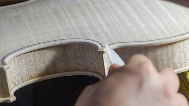 Skilled luthier hand carving violin edge with professional chisel, revealing intricate woodworking techniques during delicate instrument crafting process - Powered by Adobe