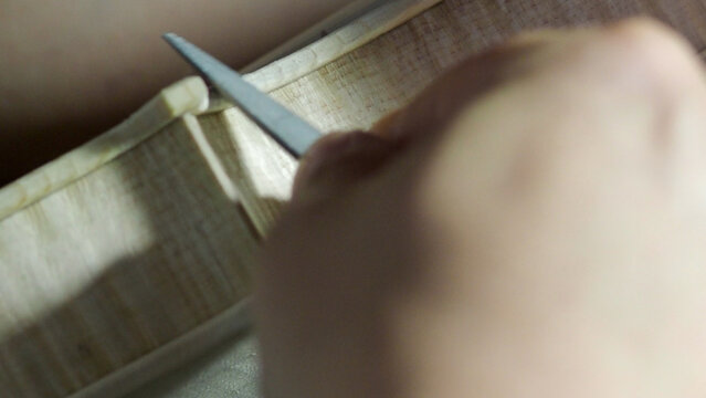 Skilled luthier carefully carving intricate purfling edges on violin, highlighting delicate woodworking techniques and artisan craftsmanship in musical instrument construction