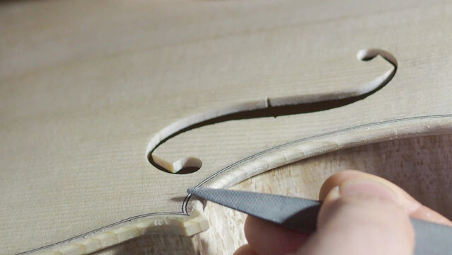 Experienced luthier carefully filing delicate f hole curve on violin, revealing intricate woodworking skill and traditional craftmanship in musical instrument construction - Powered by Adobe