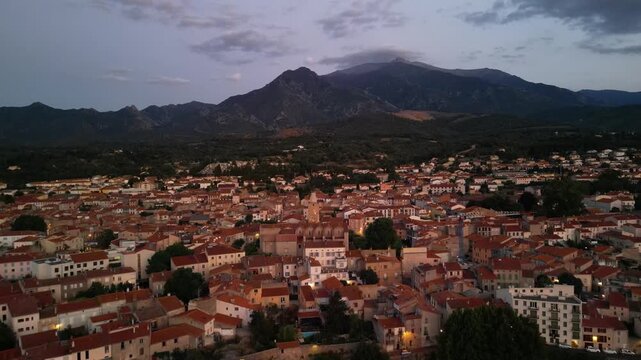 Aerial view of the city of Prades, where terracotta roofs contrast with the dark green hills and mountains, a tranquil scene, Prades, Occitanie, France.