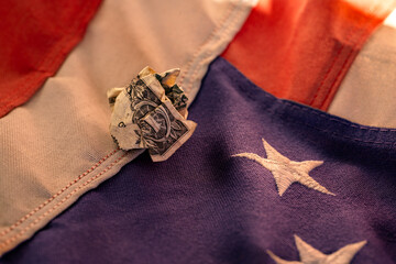 Crumpled U.S. dollar bill on American flag, symbolizing economic struggle and financial challenges...