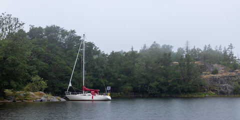 Small sail boat moored to coastal rocks, resting quietly in calm water. The rustic maritime...