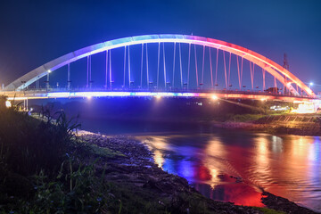 A beautiful bridge with colorful lights stretches over a calm river at night.