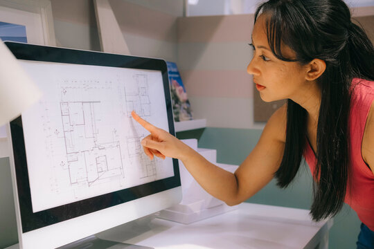Architect analyzing blueprints on computer monitor in office setting