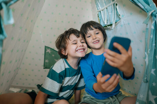 Brothers taking selfie with smartphone inside play tent at home