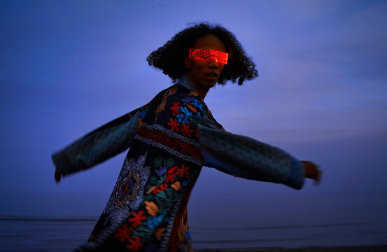 Person dancing outdoors in patchwork robe and VR glasses at dusk