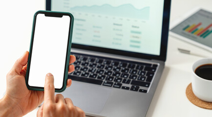 Digital banking and mobile technology. Hands holding smartphone with blank screen against laptop with financial interface