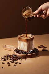 Coffee pouring into a glass cup with coffee beans on brown background