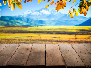 A wooden table surface in the foreground, autumn leaves in shades of yellow and orange in the...