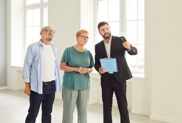 A senior couple listens to a real estate agent in an empty apartment, exploring potential purchase....
